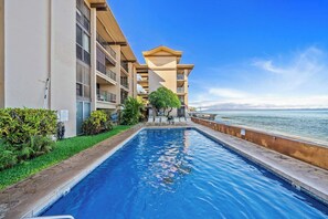 A swimming pool with a view of the sea, surrounded by a building with multiple balconies and a garden area. - 2BD Oceanfront Condo With Pool Near Beach-nohonani 105 (Napili-Honokowai)