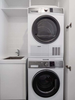A stacked washer and dryer unit in a white-walled laundry room with a sink and a door. - The Riverside Wander, Noosaville (Noosaville)