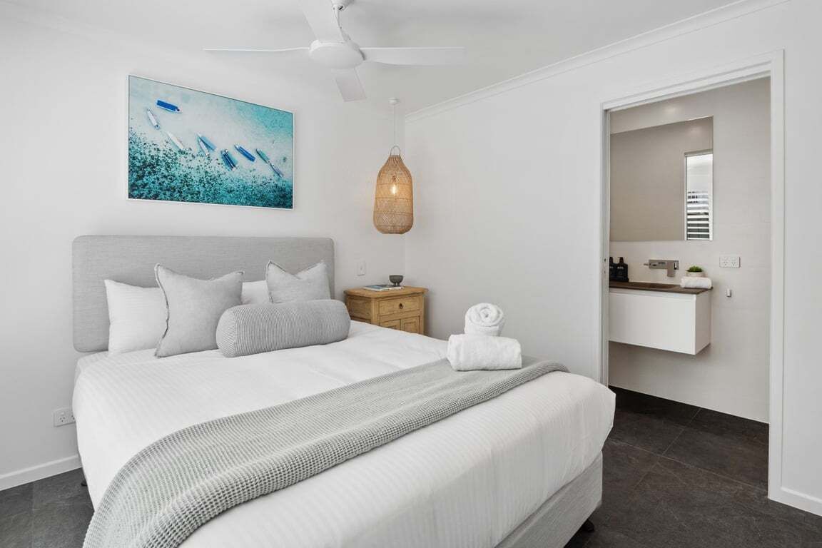 A hotel room with a bed, a bedside table, a hanging light fixture, a wall-mounted mirror, and a painting.