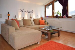 Ein Wohnzimmer mit einer Eckcouch, einem Glastisch und einem roten Teppich.
