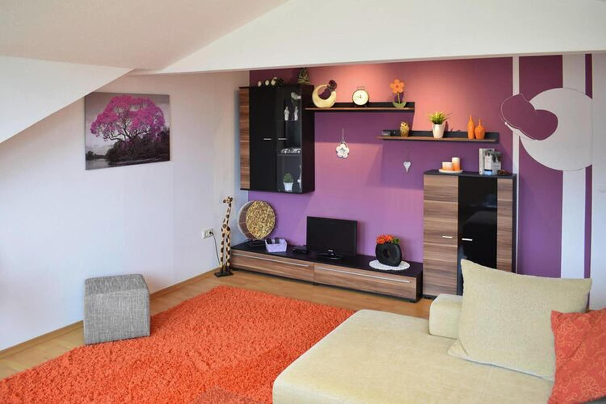 Ein modernes Wohnzimmer mit schräg verlaufender Decke, einer Couch, einem Couchtisch und einem Fernseher.