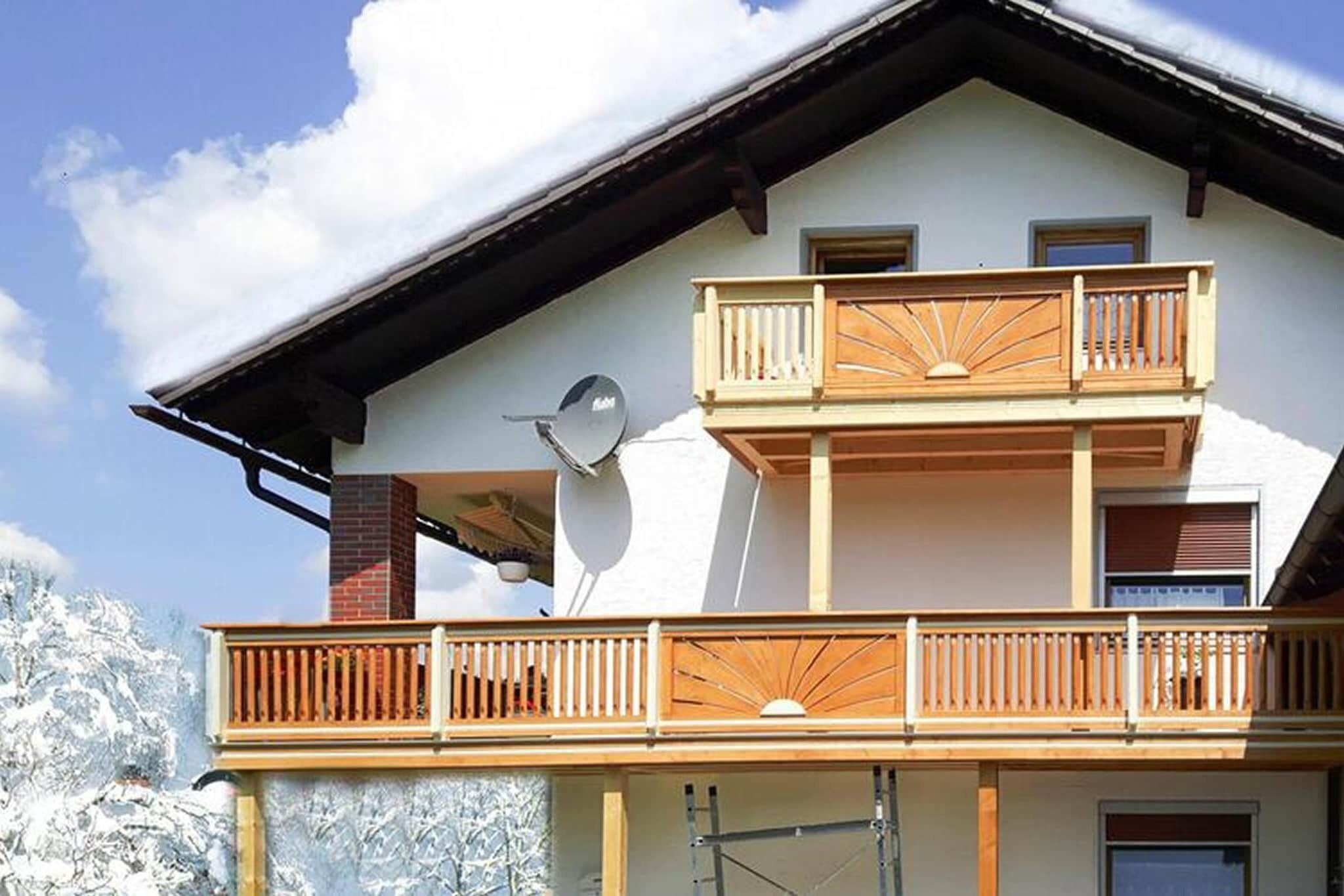 Ein zweistöckiges Gebäude mit einem Balkon im oberen Geschoss, einer Satellitenschüssel an der Seite und einem verschneiten Berg im Hintergrund.