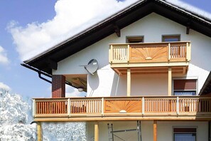 Een gebouw met twee verdiepingen, een balkon op de bovenverdieping, een schotelantenne aan de zijkant en een besneeuwde berg op de achtergrond.