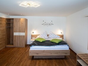 A bedroom with a wooden bed, two green pillows, a white pillow with a floral pattern, and a wall with a light fixture and a sign. - Studio - Eiblhof, Austria (Schladming)