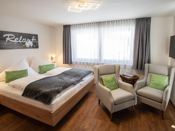A hotel room with a bed, two armchairs, a bedside table, a large window with curtains, and a wall-mounted artwork with the word "Relax". - Studio - Eiblhof, Austria (Schladming)