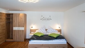 Un dormitorio con una cama de madera, dos almohadas verdes, una almohada blanca con estampado floral y una pared con una lámpara y un cartel.