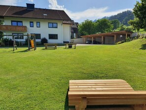 A grassy outdoor area with a wooden bench, a swing set, and a building with a covered carport. - Studio - Eiblhof, Austria (Schladming)