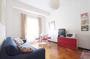 Ein Wohnzimmer mit einer Couch, einem Esstisch mit Stühlen, einem Fernseher, einer Mikrowelle und einem roten Schrank.