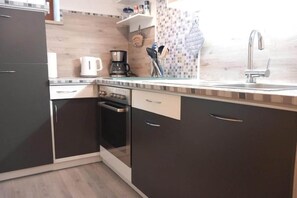 Une cuisine avec des meubles de rangement de couleur sombre, une cuisinière, une machine à café et un évier.