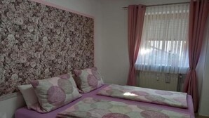 A bedroom with a floral wallpaper, a bed with a patterned bedspread, and pink curtains. - Apartment in Bodenmais near Grosser Arber (Bodenmais)