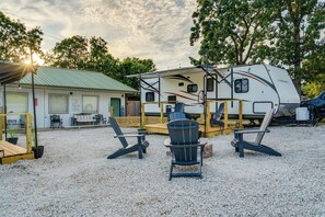 A recreational vehicle (RV) parked in a gravel area with a covered deck and outdoor seating. - 2-Unit RV Retreat Near Pomme de Terre Lake (Hermitage)