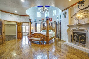 A spacious bedroom with a four-poster bed, a fireplace, and a chandelier.