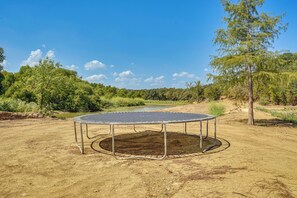 A trampoline in a natural setting with a dirt ground and trees in the background.