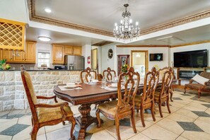 A spacious dining area with a large wooden table and ornate chairs, a kitchen with modern appliances, and a living area with a flat-screen TV.