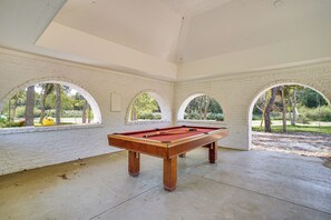 A pool table in a room with white brick walls and arched windows.