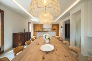 A modern dining room with a wooden table, white chairs, a central white plate, and a hanging light fixture. - Villa Na Maria: renovated finca in Porreres with private pool (Porreres)