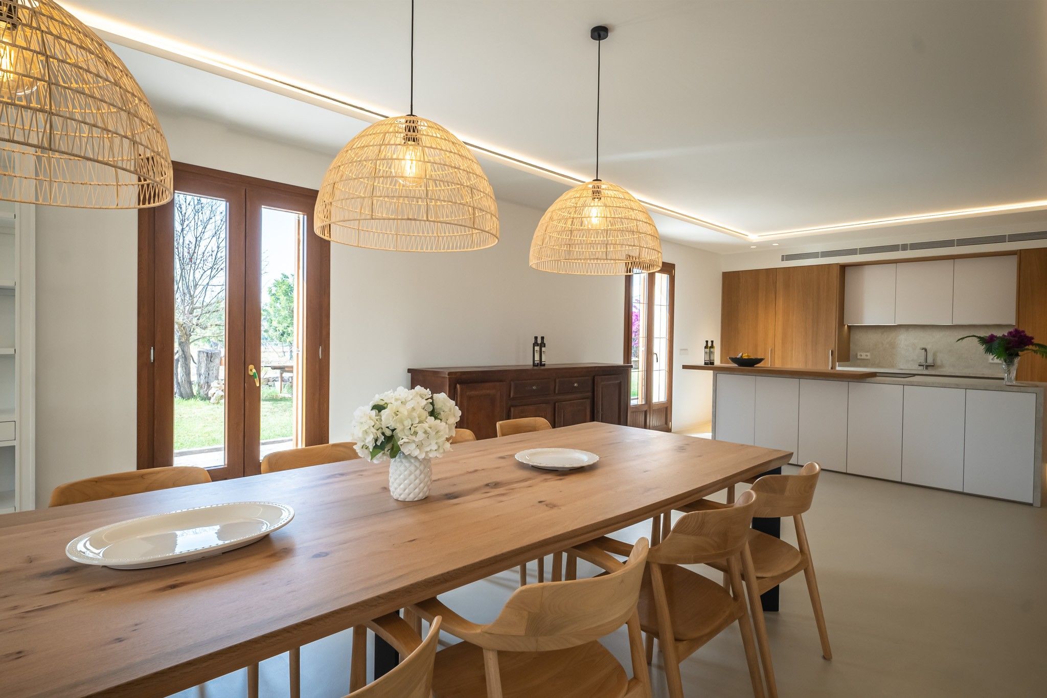 A modern kitchen with wooden cabinets, a dining table with chairs, and pendant lights.