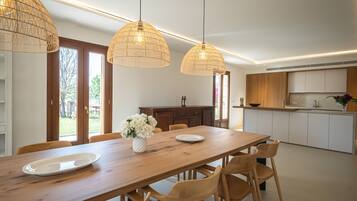 A modern kitchen with wooden cabinets, a dining table with chairs, and pendant lights.