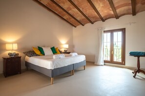 A bedroom with a bed, two bedside tables, a window with curtains, and a wooden ceiling.