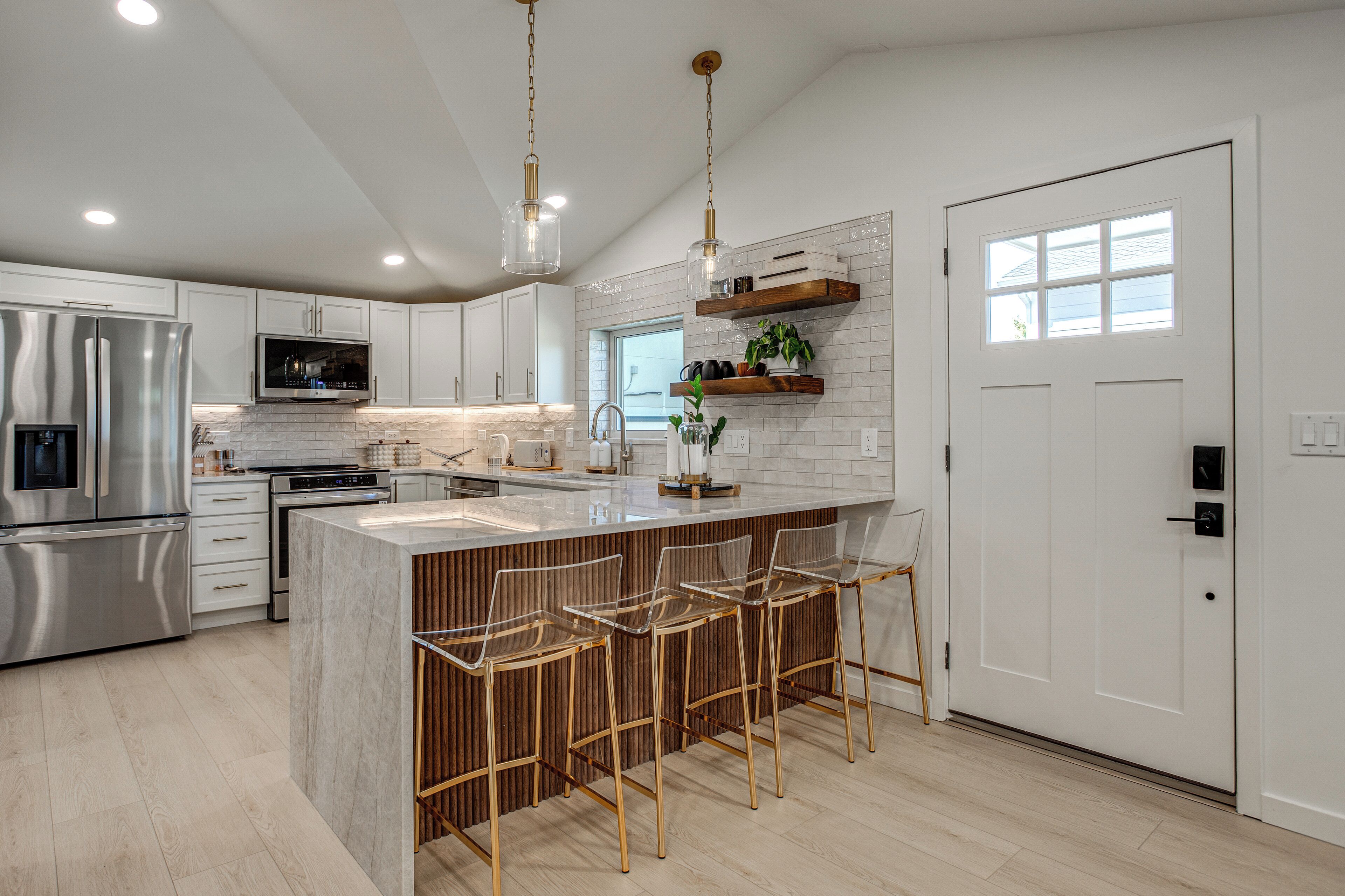 A modern kitchen with stainless steel appliances, a marble island, and bar stools.
