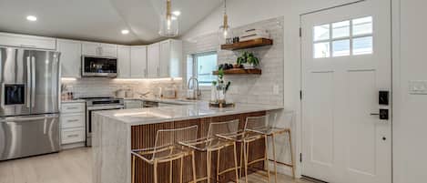 A modern kitchen with stainless steel appliances, a marble island, and bar stools.