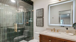 A modern bathroom with a glass-enclosed shower, a toilet, a vanity with a mirror, and framed artwork on the wall. - Mountain & Lake Views! Unit 1 Mi to Empower Field (Denver)