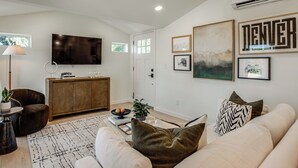 A modern living room with a flat-screen TV, a wooden cabinet, a sofa with decorative pillows, and artwork on the walls. - Mountain & Lake Views! Unit 1 Mi to Empower Field (Denver)