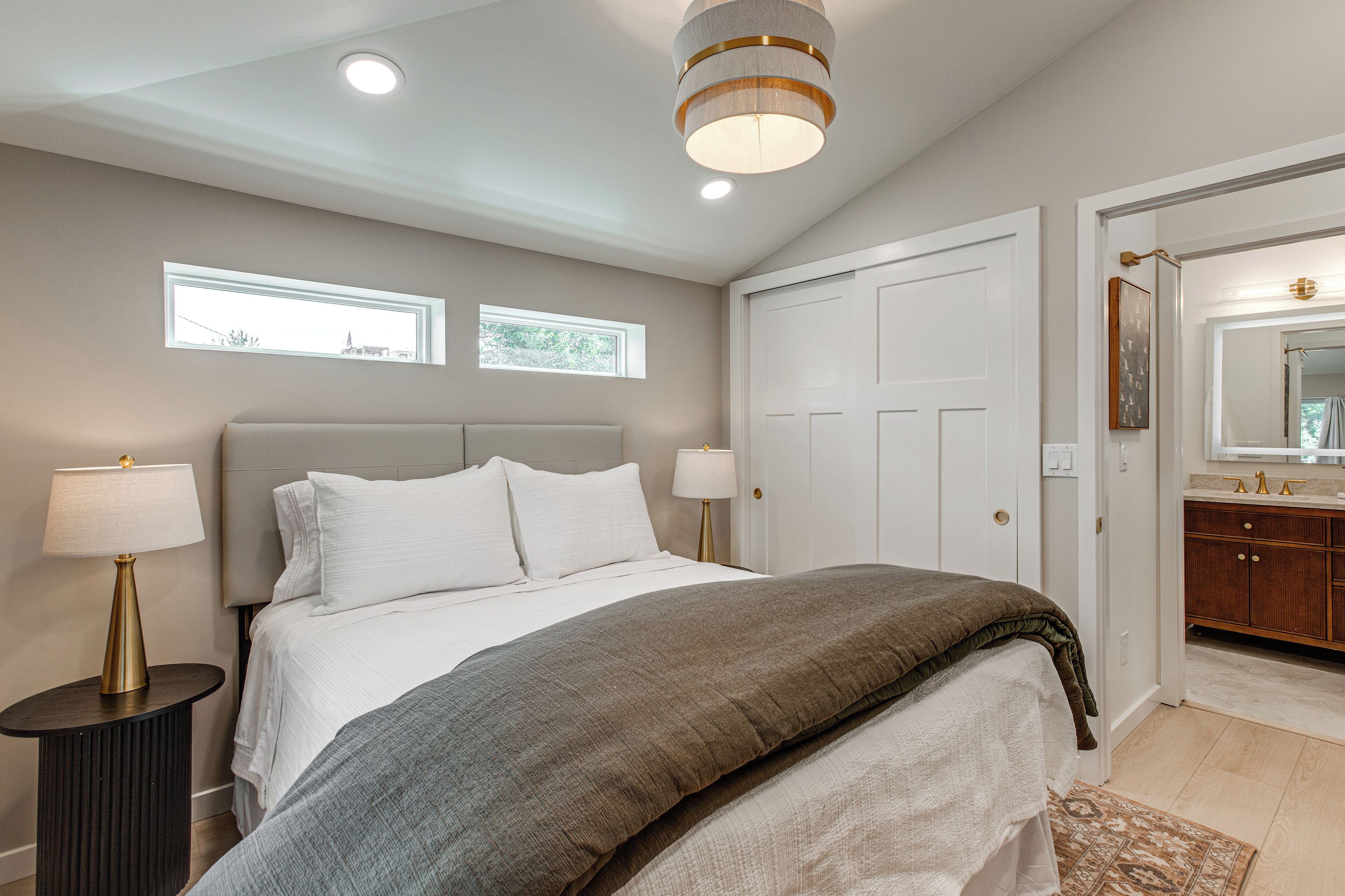 Een slaapkamer met een bed, nachtlampen, een raam en een deur naar een badkamer.
