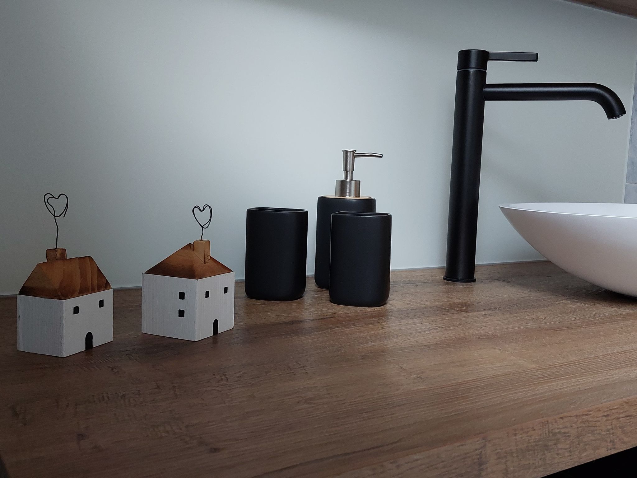 Un meuble-vasque de salle de bain avec un robinet noir, un lavabo blanc et trois récipients cylindriques.