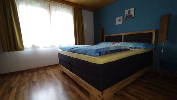 Ein Schlafzimmer mit einem Bettgestell aus Holz, einem Fenster mit Vorhängen und einer blauen Wand.