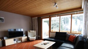 Ein Wohnzimmer mit Fernseher, einer Couch und einem großen Fenster.