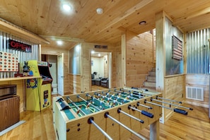 A wooden-floored room with a foosball table, a Pac-Man arcade machine, and a sign indicating a movie theater. - Mtn Views, Hot Tub, & Theater! Sevierville Gem (Sevierville)