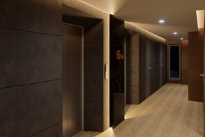 Un pasillo con paredes oscuras, un muro decorativo de mármol y una puerta de madera.