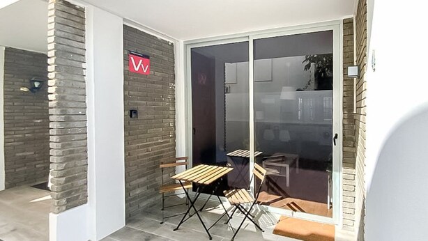 Un patio couvert avec un mur en briques, une porte-fenêtre coulissante et une table avec des chaises.