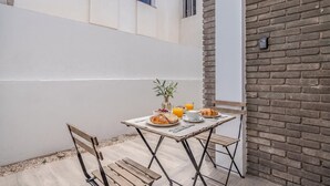 Un petit espace extérieur aménagé pour prendre les repas, avec une table pour deux, un banc et un mur en briques.