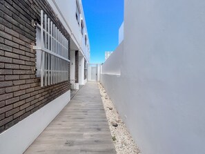 A narrow pathway flanked by a brick wall and a white wall, leading to a building with a door. - GuestReady La Garita Bay 3 (Telde)