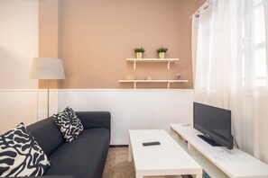 Moderni olohuone, jossa on sohva, sohvapöytä, televisio ja hyllyjä, joilla on koriste-esineitä.