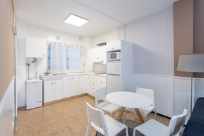 Une cuisine compacte avec des meubles blancs, un four à micro-ondes et un évier. On y trouve une table ronde avec des chaises et une lampe.