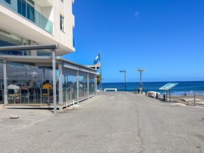 A coastal walkway with a glass-enclosed restaurant, a clear view of the sea, and a flag. - GuestReady La Garita Bay 3 (Telde)