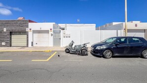 Un espace de stationnement où sont garés un scooter et une voiture devant un immeuble dont la porte de garage est visible.