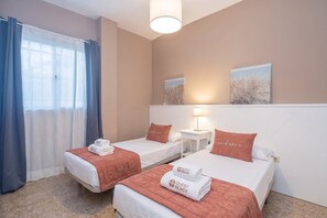 A hotel room with two beds, a window with curtains, a bedside table with a lamp, and artwork on the wall. - GuestReady La Garita Bay 3 (Telde)