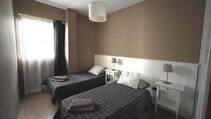 Une chambre avec deux lits, une table de chevet, une lampe et une fenêtre avec des rideaux.