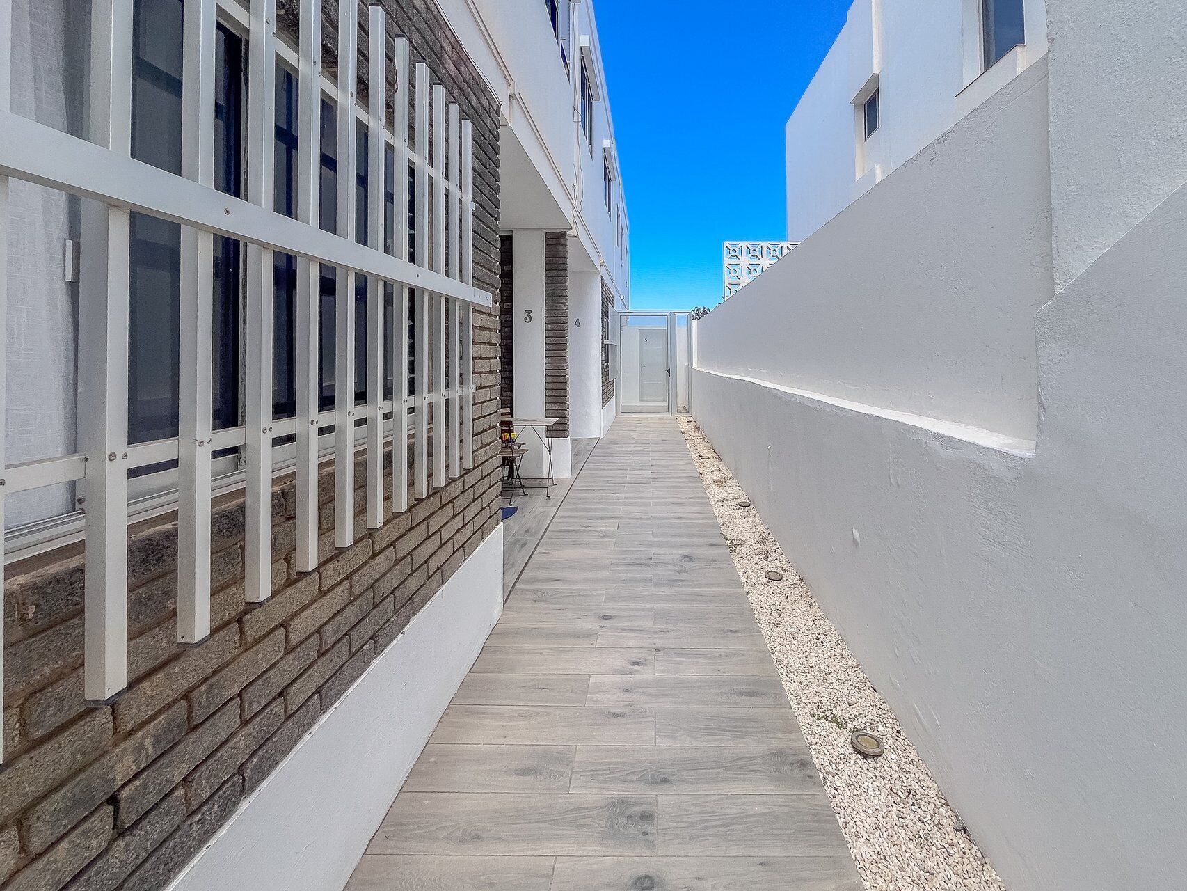 A narrow corridor with a wooden floor, white walls, and a brick section on the left.