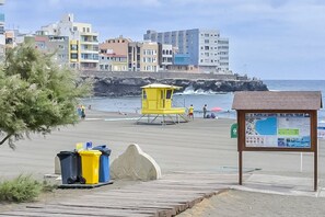Ein Strand mit einem Rettungsturm, einer Mülltonne und einem Hinweisschild.
