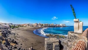 Un paysage urbain côtier avec une plage de sable, une côte rocheuse et un ciel bleu dégagé.