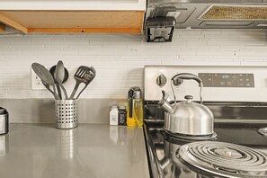 A kitchen with a stainless steel stove, a kettle, and a utensil holder with salt and pepper shakers. - New 6BR Two Unit - Perfect for Large Groups (Indianapolis)