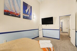 A hotel room with a bed, a flat-screen TV mounted on the wall, and two paintings depicting sailboats. - New 6BR Two Unit - Perfect for Large Groups (Indianapolis)