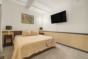 A hotel room with a bed, a painting on the wall, a flat-screen TV, and two bedside tables with lamps. - New 6BR Two Unit - Perfect for Large Groups (Indianapolis)
