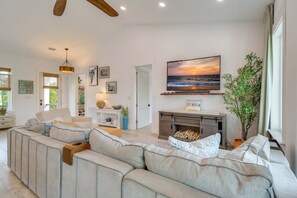 A modern living room with a sectional sofa, a fireplace, and a large TV screen displaying a sunset. - Fort Morgan Hideaway Hot Tub | Golf | Beach Access (Gulf Shores)
