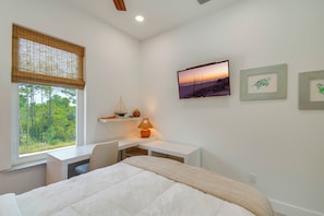 A bedroom with a bed, a desk, a chair, a window with a view of trees, and artwork on the wall. - Fort Morgan Hideaway Hot Tub | Golf | Beach Access (Gulf Shores)
